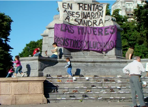 Fotografía de la manifestación con motivo del Día Internacional de lucha contra la violencia hacia las mujeres 2007. Lugar: Plaza Italia. En la fotografía puede verse una intervención en las escalinatas del monumento principal de la plaza con zapatos de distinta clase y carteles no legibles en la imagen